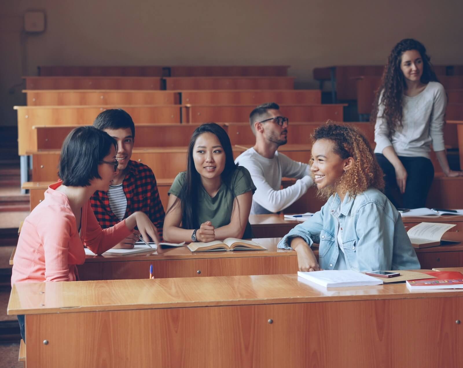 Group of students sitting in a lecture hall, talking and smiling while studying together 