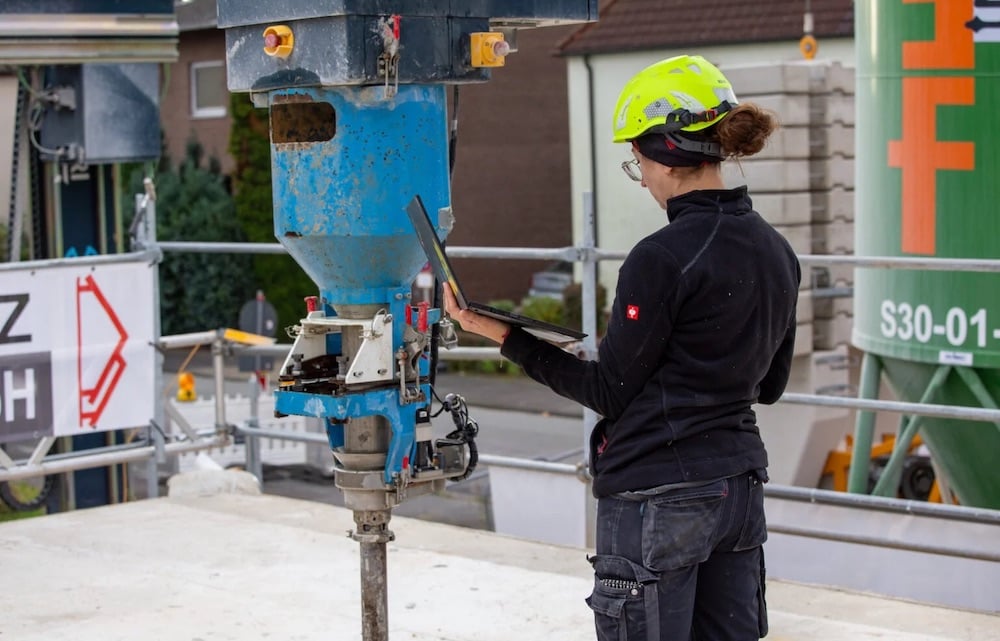 Female-presenting worker in a hard hat with a laptop controlling a 3D concrete printer