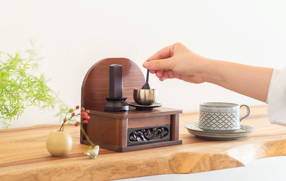 Hand striking a ceremonial singing bowl on a tiny shrine